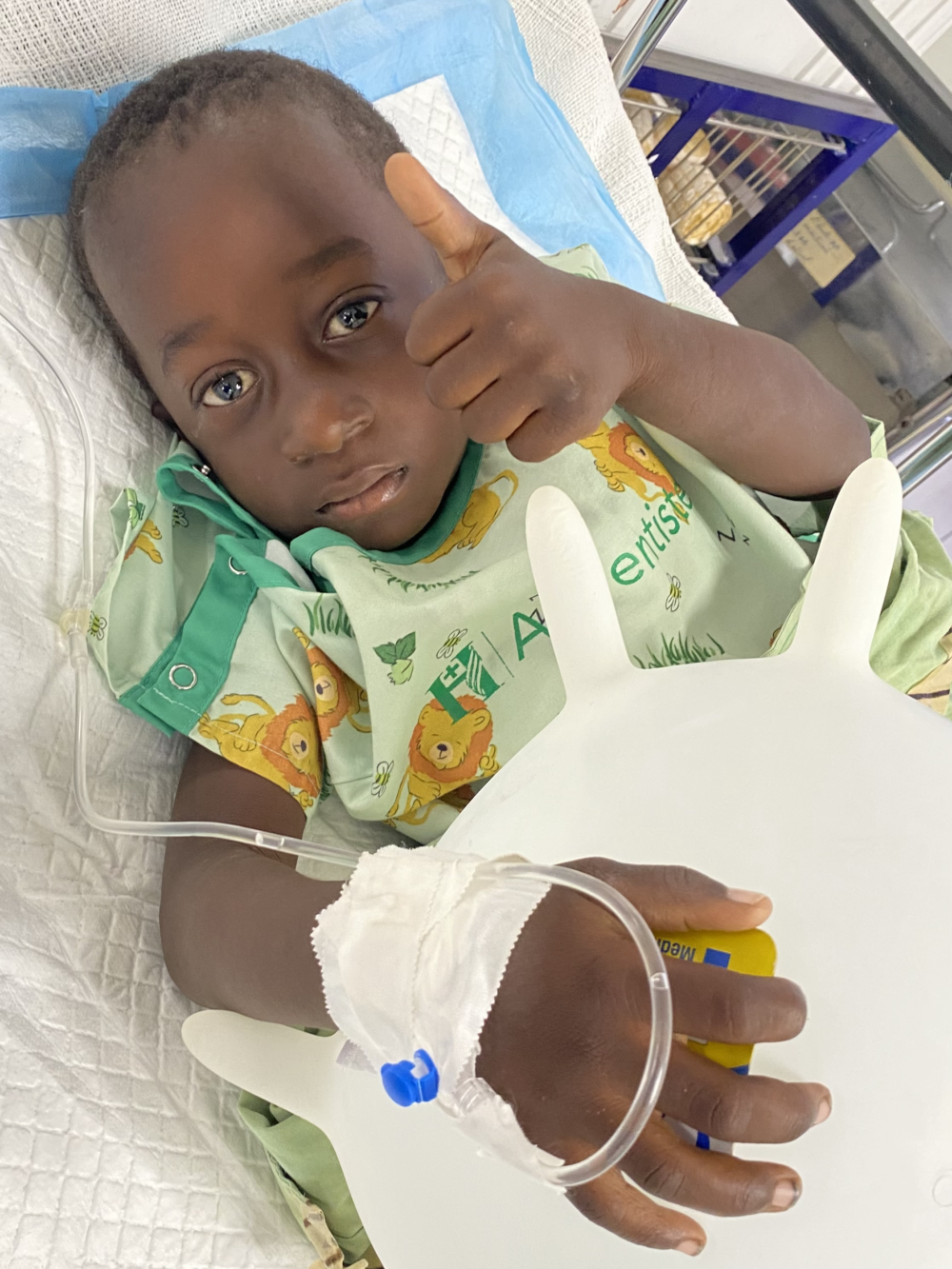 child in a hospital bed gives a thumbs up