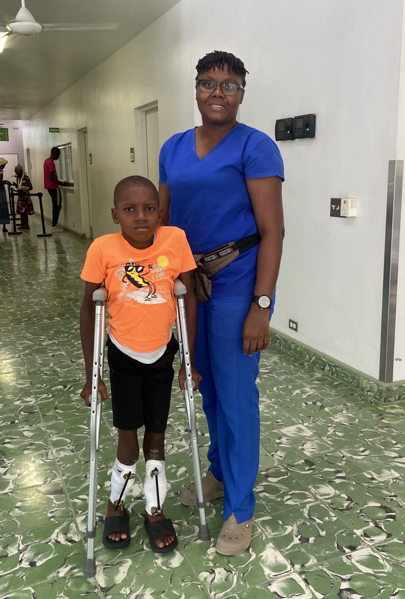 boy with braces on his legs and using crutches stands next to a physical therapist 